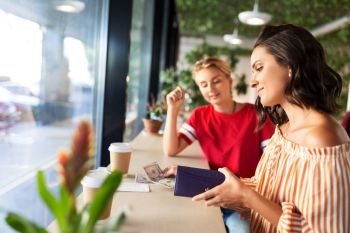 people, cash payment and finances concept - female friends paying in dollar money for coffee at cafe. female friends paying for coffee at cafe