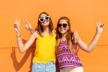 fashion, leisure and people concept - smiling teenage girls in summer clothes hugging and showing peace hand sign outdoors. smiling teenage girls showing peace in summer