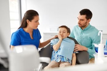 medicine, dentistry and healthcare concept - father and son suffering from toothache visiting dentist at dental clinic. father and son visiting dentist at dental clinic