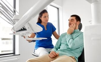 medicine, dentistry and healthcare concept - female dentist and male patient suffering from toothache at dental clinic. man with toothache and dentist at dental clinic