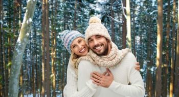 winter, christmas and people concept - happy couple in hats and scarf hugging over forest background. couple hugging over winter forest background