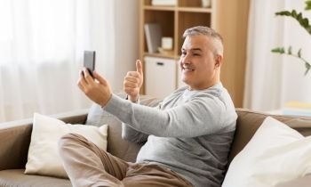 technology, people and communication concept - happy man having video chat on smartphone at home and showing thumbs up. man having video chat on smartphone at home