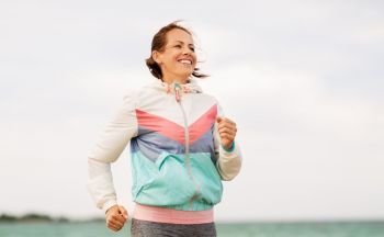 fitness, sport and healthy lifestyle concept - smiling woman running along beach. smiling woman running along beach