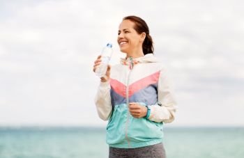 fitness, sport and healthy lifestyle concept - woman drinking water after exercising at seaside. woman drinking water after exercising at seaside