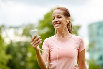 fitness, sport and healthy lifestyle concept - smiling woman listening to music on smartphone at city park in summer. woman listening to music on smartphone at park