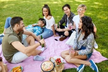 friendship and leisure concept - group of happy friends with non alcoholic drinks and food at picnic in summer park. happy friends with drinks at picnic in summer park