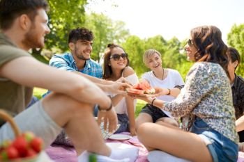 friendship, leisure and food concept - group of happy friends sharing watermelon at picnic in summer park. happy friends sharing watermelon at summer picnic