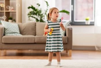 childhood and family concept - little girl blowing soap bubbles at home. little girl blowing soap bubbles at home