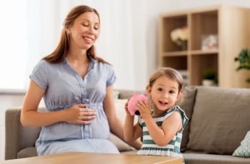 pregnancy, finances and family concept - happy pregnant mother and little daughter with piggy bank at home. pregnant mother and daughter with piggy bank