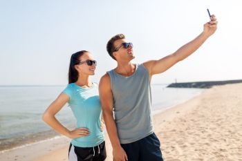 fitness, sport and lifestyle concept - happy couple in sports clothes taking selfie by smartphone on beach. couple taking selfie by smartphone on beach