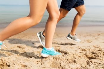 fitness, sport and technology concept - legs of couple of sportsmen in sneakers running along summer beach. legs of sportsmen in sneakers running along beach