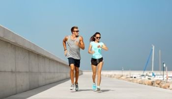 sport, technology and lifestyle concept - happy couple with fitness tracker running along pier in summer. couple with fitness tracker running along pier