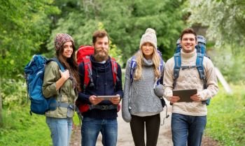 travel, technology and hiking concept - group of smiling friends or travelers with backpacks and tablet pc computers outdoors. friends or travelers with backpacks and tablet pc