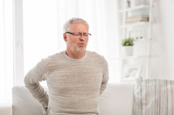 people, health care and problem concept - unhappy senior man suffering from pain in back or reins at home. unhappy senior man suffering from backache at home