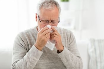 healthcare, flu, hygiene and people concept - sick senior man with paper wipe blowing his nose at home. sick senior man with paper wipe blowing his nose