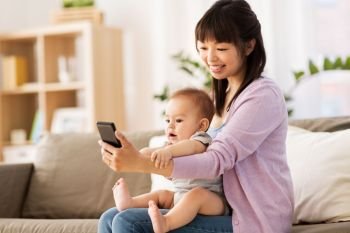 family and motherhood concept - happy smiling young asian mother with little baby son taking selfie by smartphone at home. asian mother with baby son taking selfie at home
