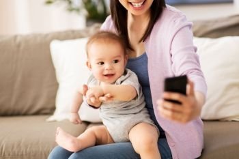 family and motherhood concept - happy smiling young asian mother with little baby son taking selfie by smartphone at home. mother with baby taking selfie at home