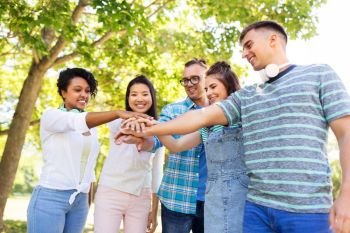 people, friendship and international concept - group of happy smiling friends stacking hands in park. happy smiling friends stacking hands in park