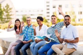 education, international and people concept - group of happy exchange students with notebook and takeaway drinks waving hands outdoors. students with notebook waving hands outdoors