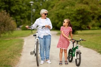 family, leisure and people concept - happy grandmother and granddaughter with bicycles at summer park. grandmother and granddaughter with bicycles
