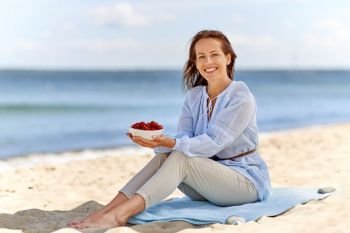 people and leisure concept - happy smiling woman holding bowl with strawberries on summer beach. woman holding bowl with strawberries on beach