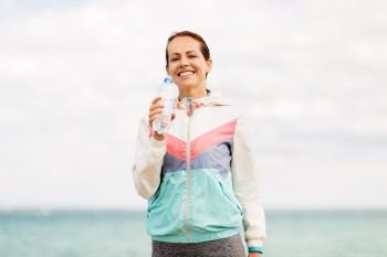 fitness, sport and healthy lifestyle concept - woman drinking water after exercising at seaside. woman drinking water after exercising at seaside