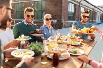leisure and people concept - happy friends eating and drinking at barbecue party on rooftop in summer. happy friends eating at barbecue party on rooftop