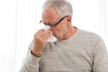 healthcare, flu, hygiene and people concept - sick senior man with paper wipe blowing his nose at home. sick senior man with paper wipe blowing his nose
