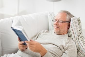 old age, leisure and people concept - senior man lying on sofa and reading book at home. senior man lying on sofa and reading book at home