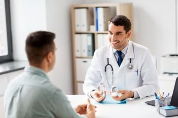 medicine, healthcare and diabetes concept - smiling doctor with glucometer and insulin pen device talking to male patient at medical office in hospital. doctor with glucometer and patient at hospital