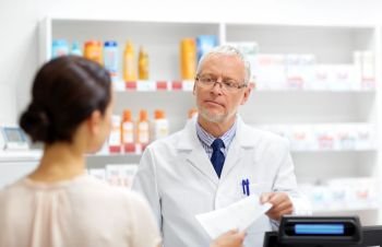 medicine, healthcare and people concept - senior apothecary taking prescription from customer at drugstore. senior apothecary with prescription at pharmacy