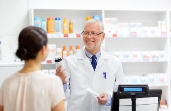 medicine, pharmaceutics, healthcare and people concept - senior apothecary with drug and prescription and female customer at pharmacy. apothecary with cure and customer at pharmacy