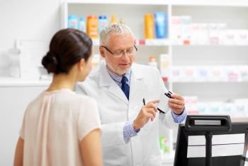 medicine, pharmaceutics, healthcare and people concept - senior apothecary with drug and female customer at pharmacy. apothecary with cure and customer at pharmacy