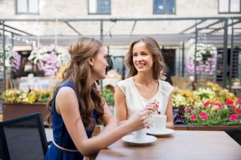 communication and friendship concept - smiling young women drinking coffee at street cafe. smiling young women drinking coffee at street cafe