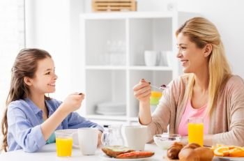 food, healthy eating, family and people concept - happy mother and daughter having breakfast at home kitchen. happy mother and daughter having breakfast at home