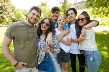 friendship, leisure and technology concept - group of happy smiling friends taking picture by selfie stick at summer park. friends taking picture by selfie stick at summer