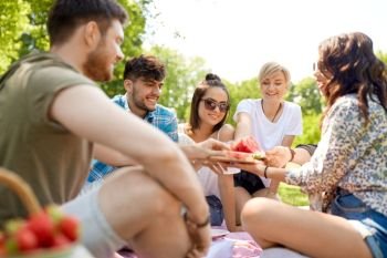 friendship, leisure and food concept - group of happy friends sharing watermelon at picnic in summer park. happy friends sharing watermelon at summer picnic