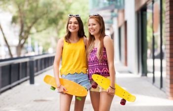 friendship, leisure and people concept - happy teenage girls or friends with short skateboards on city street in summer. teenage girls with short skateboards in city