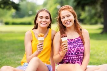 leisure and friendship concept - happy smiling teenage girls or friends eating ice cream at picnic in summer park. teenage girls eating ice cream at picnic in park