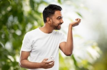 male perfumery, grooming and people concept - happy smiling young indian man smelling perfume over green natural background. happy indian man with perfume