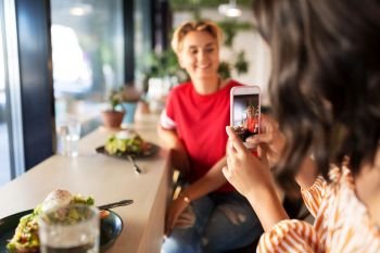 leisure, technology and people concept - female friends having lunch and photographing by smartphone at restaurant or cafe. women having lunch and photographing at cafe