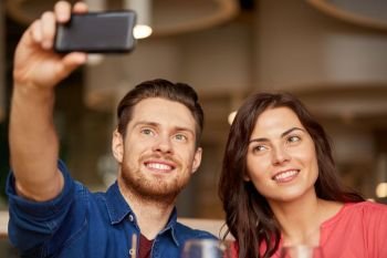 leisure, technology and people concept - happy couple taking selfie by smartphone at restaurant. couple taking selfie by smartphone at restaurant