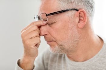 stress, old age and people concept - close up of senior man in glasses having headache and massaging nose bridge. senior man in glasses massaging nose bridge