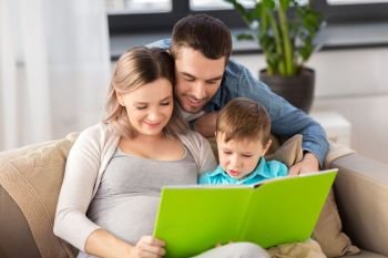 pregnancy, people and family concept - happy pregnant mother, father and little son reading book on sofa at home. happy family reading book at home