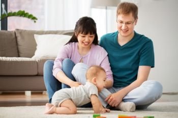 mixed race family, parenthood and people concept - happy mother, father and baby boy playing toy blocks at home. happy mixed race family with baby son at home