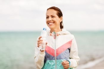 fitness, sport and healthy lifestyle concept - woman drinking water after exercising on beach. woman drinking water after exercising on beach