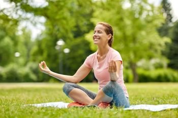 fitness, yoga and healthy lifestyle concept - happy woman meditating in summer park. happy woman meditating in summer park