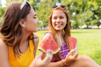 leisure and friendship concept - happy smiling teenage girls or friends eating watermelon at picnic in summer park. teenage girls eating watermelon at picnic in park