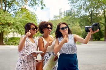 tourism, travel and technology concept - happy women with city guide and map recording video blog by camera in summer park and showing thumbs up. women with map travelling and recording video blog