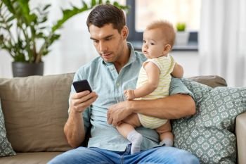 family, fatherhood and technology concept - father with little baby daughter using smartphone at home. father with baby daughter using smartphone at home